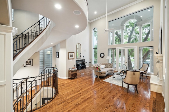 living area featuring crown molding, a ceiling fan, a high ceiling, and wood finished floors