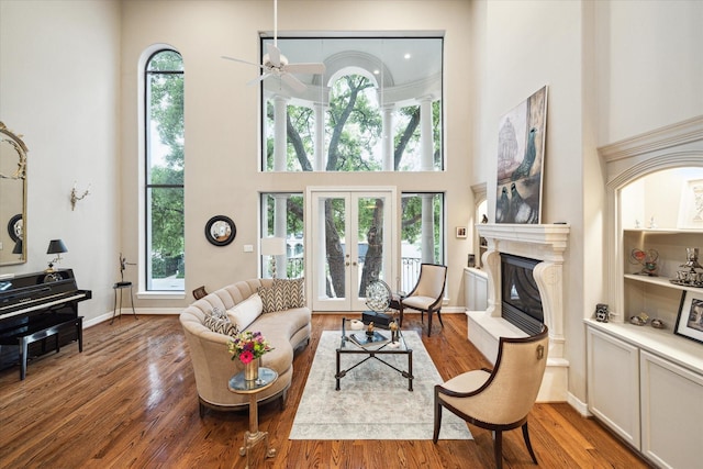 living area with french doors, a high ceiling, a ceiling fan, wood finished floors, and a premium fireplace
