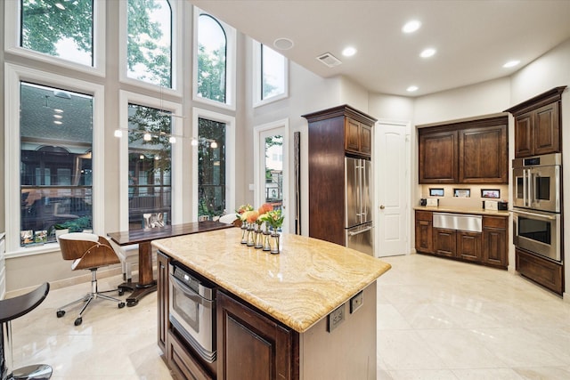 kitchen with a kitchen island, dark brown cabinetry, a warming drawer, and appliances with stainless steel finishes