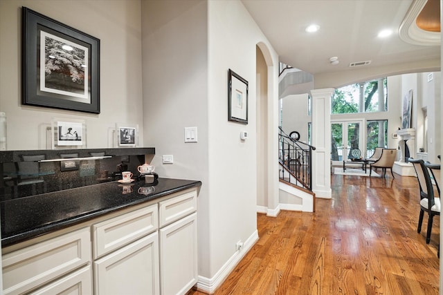 hall featuring visible vents, baseboards, arched walkways, and light wood-style floors