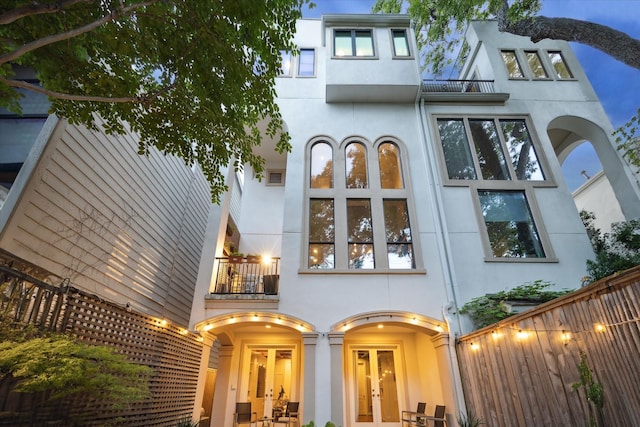 back of house featuring french doors, stucco siding, fence, and a balcony