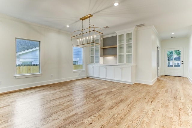 unfurnished dining area featuring a chandelier, ornamental molding, visible vents, and light wood-style flooring