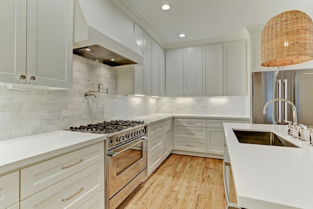 kitchen with a sink, light countertops, light wood-type flooring, stainless steel appliances, and custom range hood