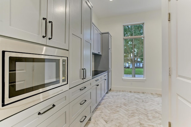 kitchen featuring stainless steel microwave, gray cabinetry, and baseboards