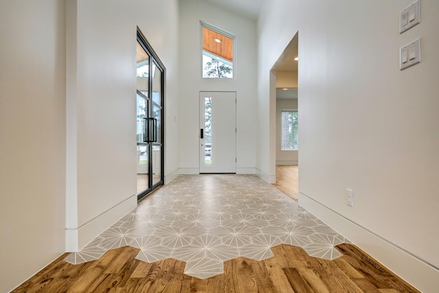 entrance foyer with light wood-style floors, a towering ceiling, and baseboards