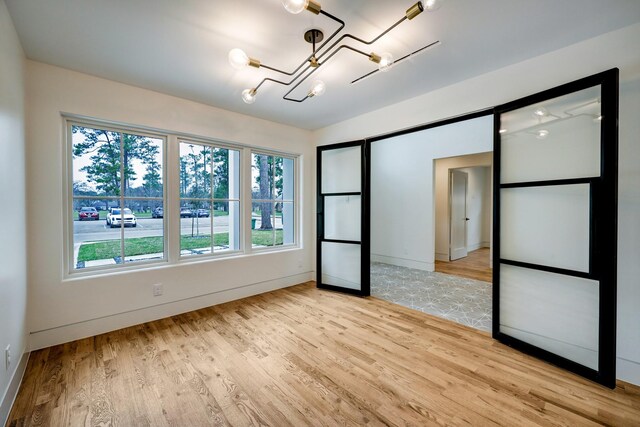spare room featuring light wood finished floors, baseboards, and an inviting chandelier