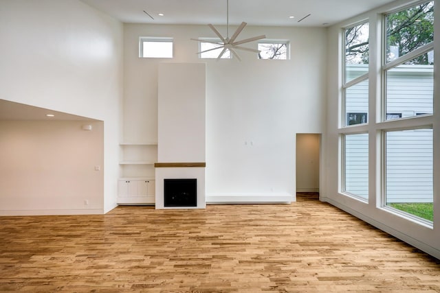 unfurnished living room featuring wood finished floors, a towering ceiling, and a healthy amount of sunlight