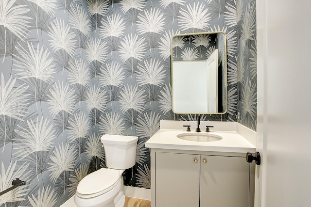 bathroom with toilet, wallpapered walls, and vanity