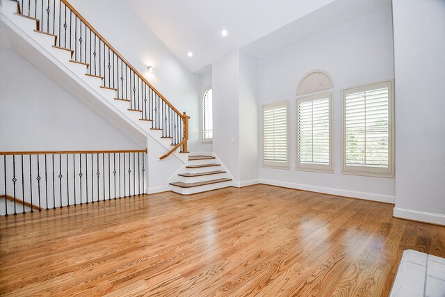unfurnished living room with baseboards, recessed lighting, a towering ceiling, wood finished floors, and stairs