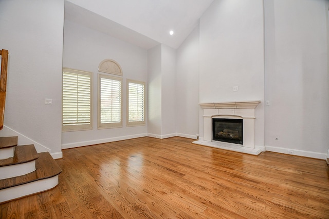 unfurnished living room with baseboards, stairway, wood finished floors, high vaulted ceiling, and a glass covered fireplace