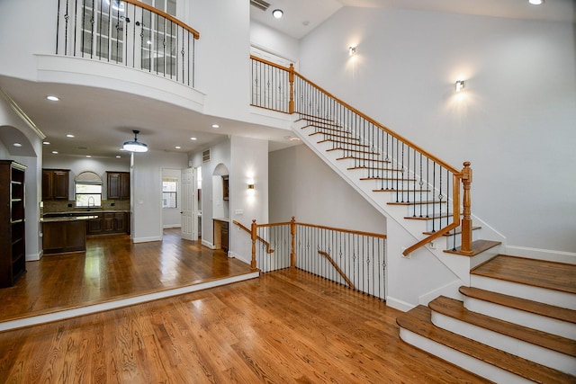 stairs with visible vents, a high ceiling, baseboards, and wood finished floors