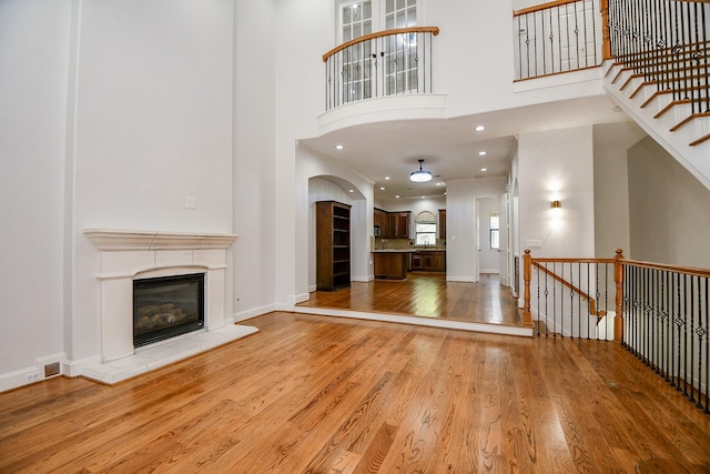 unfurnished living room with a glass covered fireplace, a towering ceiling, baseboards, and wood finished floors