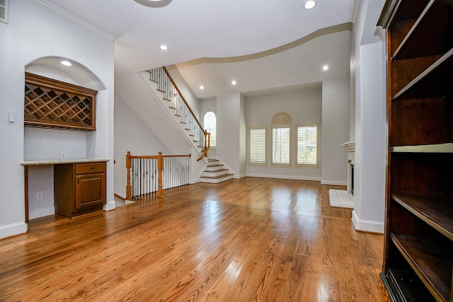 unfurnished living room featuring stairway, baseboards, a dry bar, and light wood finished floors