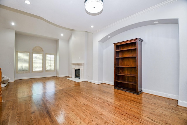 unfurnished living room with baseboards, crown molding, recessed lighting, wood finished floors, and a glass covered fireplace