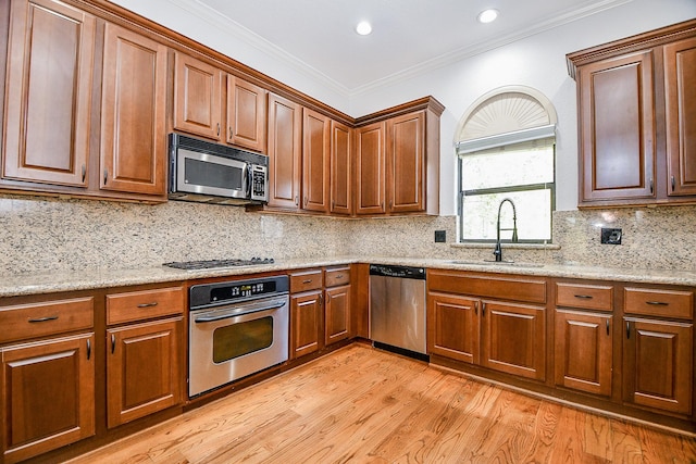 kitchen with light stone countertops, light wood-style flooring, tasteful backsplash, a sink, and stainless steel appliances