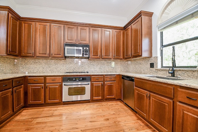 kitchen featuring light wood-style flooring, a sink, crown molding, and appliances with stainless steel finishes