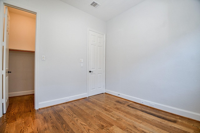 unfurnished bedroom featuring visible vents, baseboards, a walk in closet, and wood finished floors