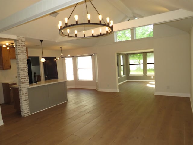 unfurnished living room featuring ornate columns, an inviting chandelier, a healthy amount of sunlight, beam ceiling, and baseboards
