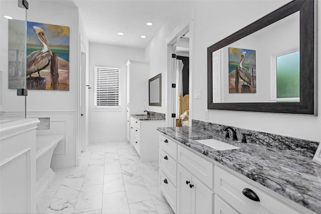 bathroom featuring recessed lighting, marble finish floor, a sink, two vanities, and a soaking tub