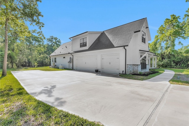 view of side of home with a yard, an attached garage, a shingled roof, and concrete driveway