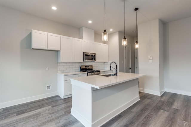 kitchen featuring tasteful backsplash, a sink, dark wood-style flooring, appliances with stainless steel finishes, and a center island with sink