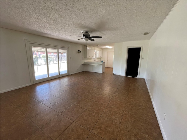 unfurnished living room featuring baseboards, a textured ceiling, a ceiling fan, and dark tile patterned flooring