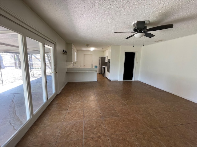 unfurnished living room with dark tile patterned floors, visible vents, a textured ceiling, and a ceiling fan