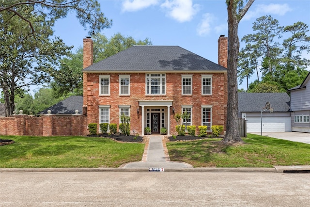 georgian-style home featuring a chimney, a front yard, driveway, and brick siding
