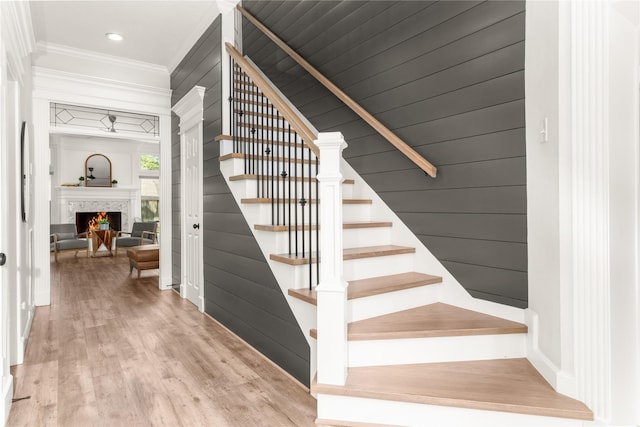 staircase featuring wood finished floors, ornamental molding, a lit fireplace, and recessed lighting