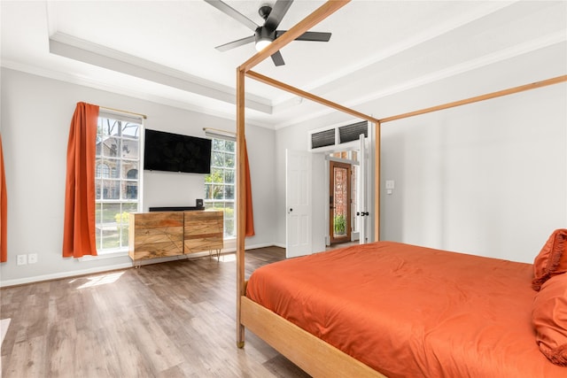 bedroom featuring a tray ceiling, ornamental molding, wood finished floors, baseboards, and ceiling fan