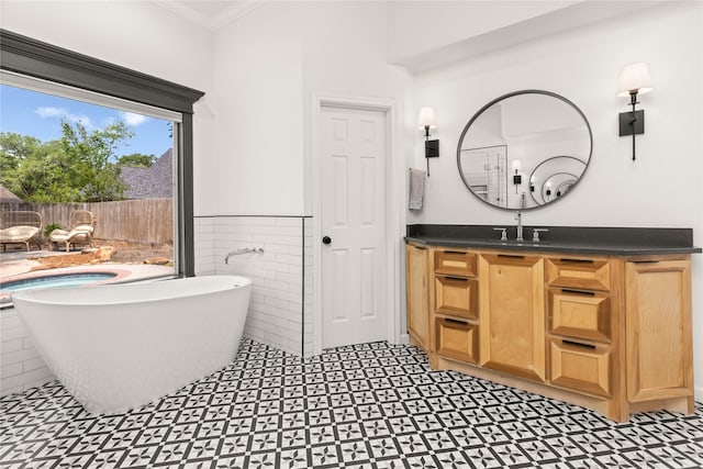 full bath featuring tile walls, vanity, a freestanding tub, wainscoting, and tile patterned floors