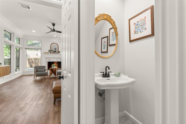 bathroom featuring a ceiling fan, baseboards, wood finished floors, crown molding, and a high end fireplace