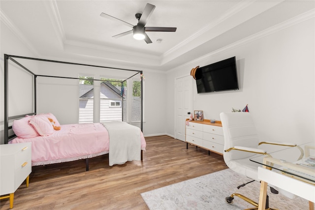 bedroom with a tray ceiling, wood finished floors, crown molding, a ceiling fan, and baseboards