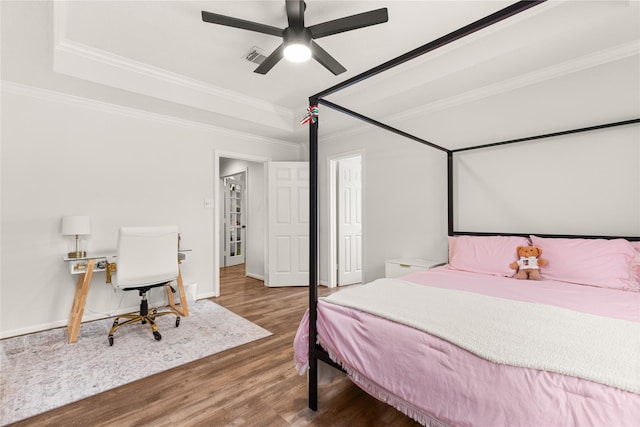 bedroom featuring wood finished floors, crown molding, a tray ceiling, a ceiling fan, and baseboards