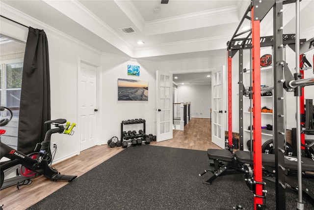 exercise room featuring wood finished floors, a tray ceiling, ornamental molding, french doors, and baseboards