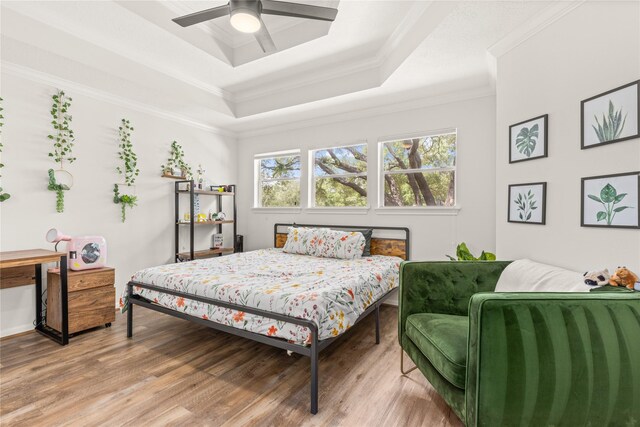 bedroom with a raised ceiling, ornamental molding, wood finished floors, and a ceiling fan