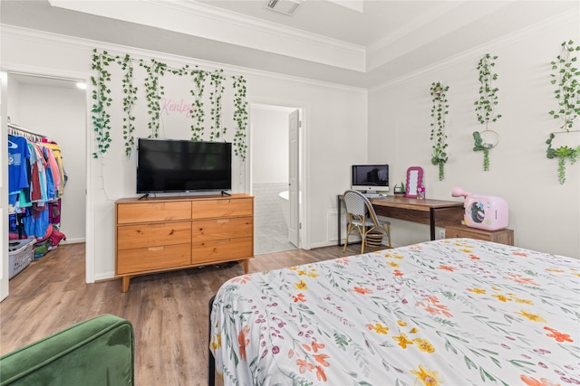 bedroom with crown molding, wood finished floors, a raised ceiling, a spacious closet, and ensuite bathroom