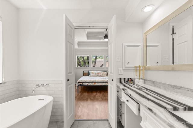 ensuite bathroom featuring a freestanding tub, vanity, a raised ceiling, a wainscoted wall, and tile walls