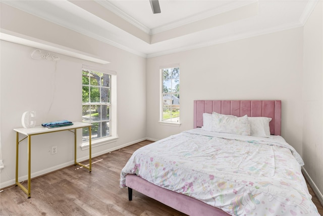 bedroom featuring wood finished floors, a raised ceiling, ornamental molding, and baseboards