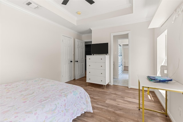 bedroom with wood finished floors, a raised ceiling, ornamental molding, baseboards, and a closet