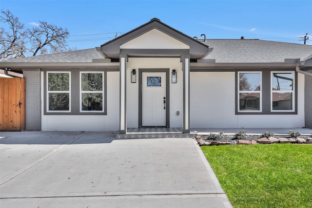 single story home with brick siding, a front lawn, stucco siding, and roof with shingles