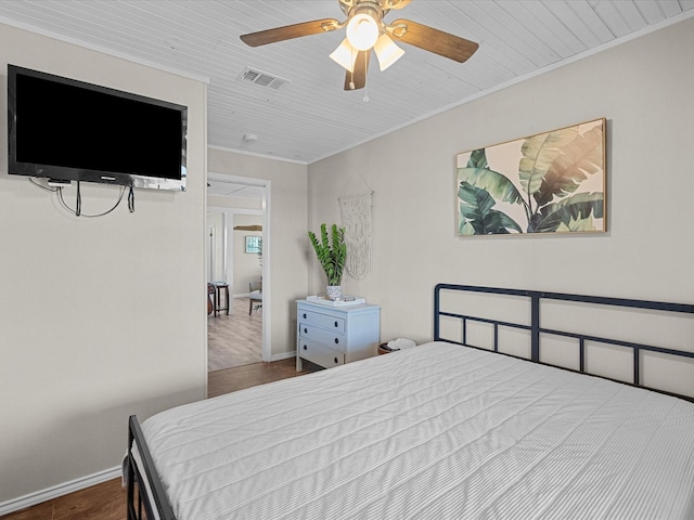 bedroom with a ceiling fan, ornamental molding, visible vents, wood finished floors, and baseboards