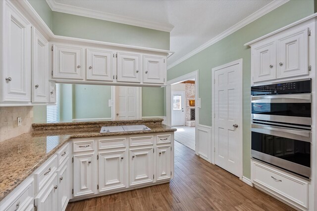 7914 Rio Crystal Dr, Houston, TX 77095 - kitchen with stainless steel double oven, crown molding, light wood-style flooring, white cabinets, and a peninsula