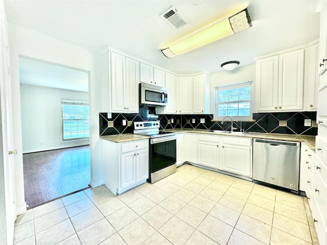 7914 Oakington Dr, Houston, TX 77071 - kitchen featuring stainless steel appliances, a sink, light tile patterned floors, tasteful backsplash, and white cabinets