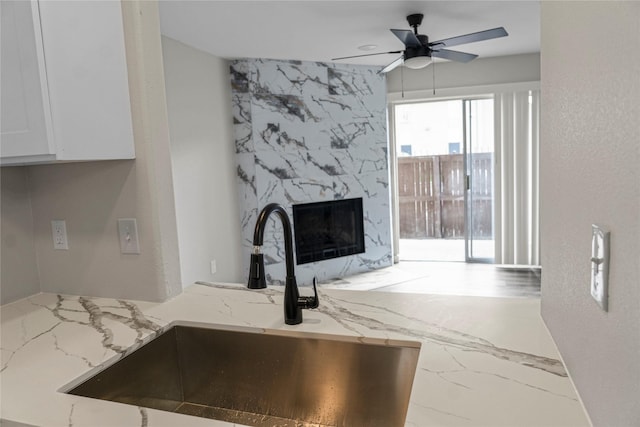 room details with light stone counters, white cabinets, ceiling fan, a high end fireplace, and a sink