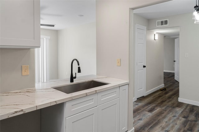 kitchen featuring light stone countertops, white cabinetry, visible vents, a sink, and dark wood-style floors