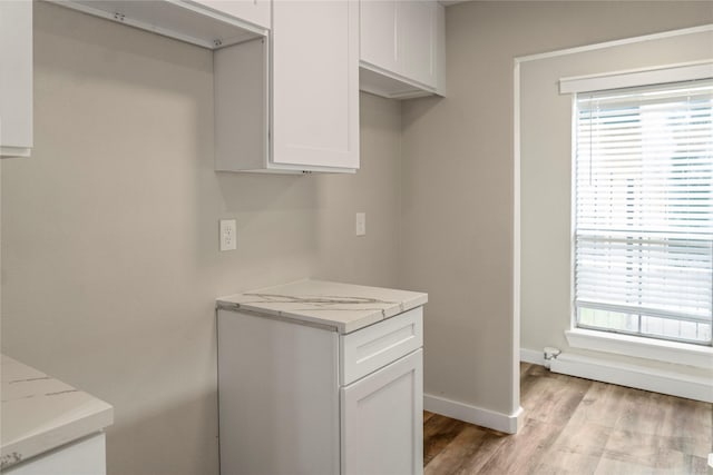 kitchen with light stone countertops, light wood finished floors, baseboards, and white cabinets