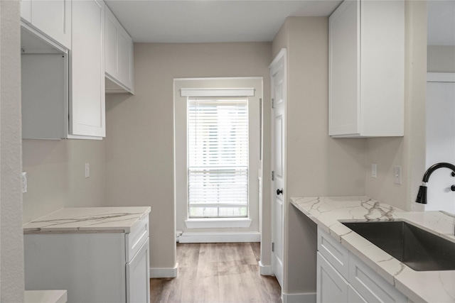 kitchen featuring light wood-type flooring, white cabinetry, light stone counters, a sink, and baseboards