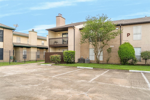 view of property with uncovered parking, central air condition unit, and fence