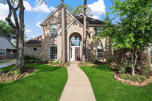view of front facade with brick siding, a shingled roof, and a front yard